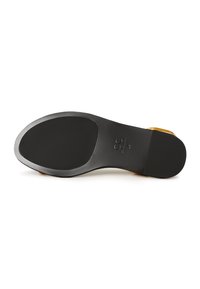 Suola in gomma nera con una finitura liscia, forma arrotondata e discreto dettaglio del logo. Accenti gialli vicino al tallone arricchiscono il design.
