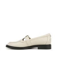 Mocassins en cuir beige avec une semelle noire plate, présentant un détail découpé et une sangle assortie sur le cou-de-pied. Texture lisse.
