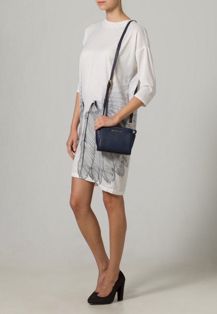 Vitt klänning med svart bladtryck, korta ärmar, tillsammans med en liten marinblå axelremsväska och svarta högklackade skor.