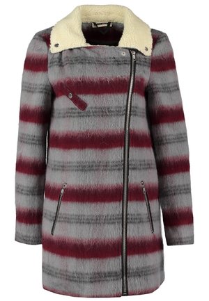 Femme portant un manteau rayé gris et bordeaux avec une doublure en polaire blanche, un jean foncé, des bottines noires et tenant un grand sac fourre-tout noir.