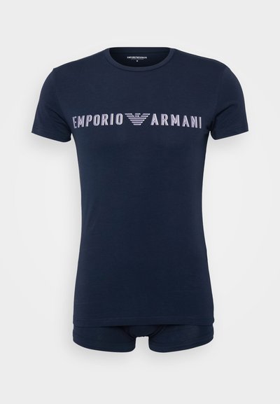 T-shirt de algodão azul-marinho com mangas curtas, apresentando um logótipo branco "EMPORIO ARMANI" atravessando o peito em uma fonte negrito e moderna.