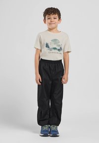 Camiseta beige claro con gráfico de montaña, pantalones negros elásticos y zapatillas azules con detalles verdes. Corte casual, diseño sencillo.