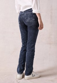 Jeans blu scuri con un design aderente, dotati di due tasche posteriori, una texture sottile e abbinati a sneakers bianche.