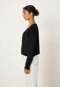 Pull noir court avec un col en V et des manches longues, présentant une texture douce. Assorti avec un pantalon en denim clair taille haute.