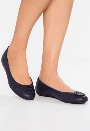 Ballerines en cuir bleu marine avec un bout arrondi et un accent logo noir prominent à l'avant. Texture lisse, design sans lacets.