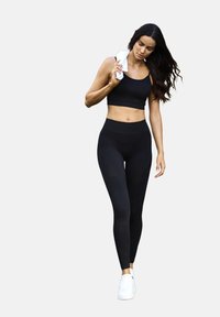 Melnā sporta krūšturis un augstās jostas bikses, abas izgatavotas no gludas, elastīgas auduma. Līdz ceļgaliem, valkātas ar baltām sporta apaviem.