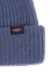 Breipet in gemêleerd blauw, met gestructureerde steken en een omgeslagen rand met een klein rood en zwart merklabel.