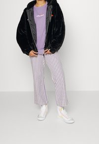 Sort faux fur jakke over en lavendel sweatshirt, parret med lilla og hvidt ternede bukser og multikolore højtop sneakers.