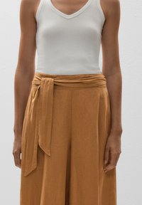 White ribbed tank top paired with high-waisted, light brown wide-leg pants featuring a tied belt and smooth, lightweight fabric.