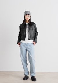 Crna kožna jakna sa četiri džepa, svijetlosiva majica, svijetloplave traperice i crne čizme na debelom đonu. Sivi beanie zaokru�žuje outfit.