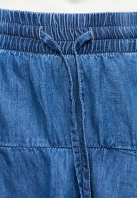 Κοντινό πλάνο μπλε τζιν παντελονιού με ελαστική μέση και δεμένο κορδόνι στο κέντρο μπροστά.