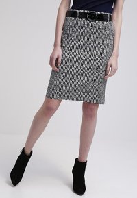 Svart och vit mönstrad knälång kjol med en figurnära design, kombinerad med ett svart bälte och ankelstövlar, mot en neutral bakgrund.