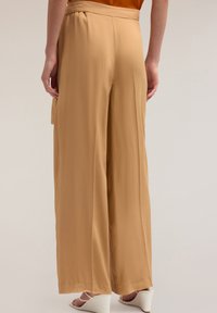 Brede pantalon in een lichtbruine stof, met een zachte textuur en een hoge taille met subtiele plooien. Zichtbare zijzakken.