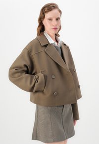 Brown cropped double-breasted jacket with large buttons and wide lapels, worn over a gray sweater and plaid skirt, showcasing a smooth texture.