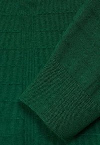 Detail eines grünen Strickpullovers, der einen strukturierten Stoff mit horizontalen Streifen zeigt. Die umgeschlagene Manschette hat eine glatte Oberfläche und einen gerippten Rand.