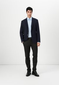 Blazer azul marino, camisa azul clara, pantalones gris oscuro y zapatos negros. El blazer tiene dos botones, la camisa tiene botones visibles y diseño ajustado.