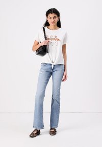 Hvid bomulds T-shirt med flamingo grafik, lyseblå flared jeans, sort crossbody taske og leopardprint sko på en model.