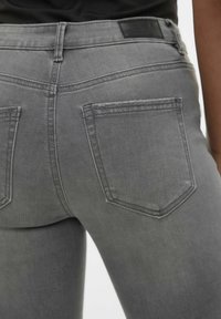Jeans de mezclilla gris con un diseño ajustado, que cuentan con dos bolsillos traseros, una textura suave y una cinturilla con una etiqueta negra.