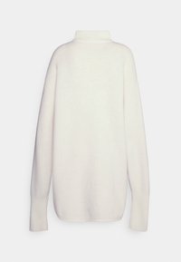 Suéter de gran tamaño en color crema con un cuello alto, puños acanalados y una textura suave. Sin patrones visibles ni herrajes.