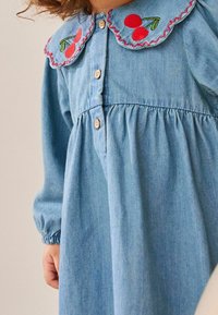 Abito in denim con vita arricciata, tessuto blu, colletto a scallop prominente, ciliegie rosse ricamate e bottoni in legno davanti.