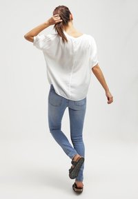 Løs siddende hvid bluse med korte ærmer, parret med lyseblå skinny jeans og brune sandaler. Glat tekstur, afslappet design.