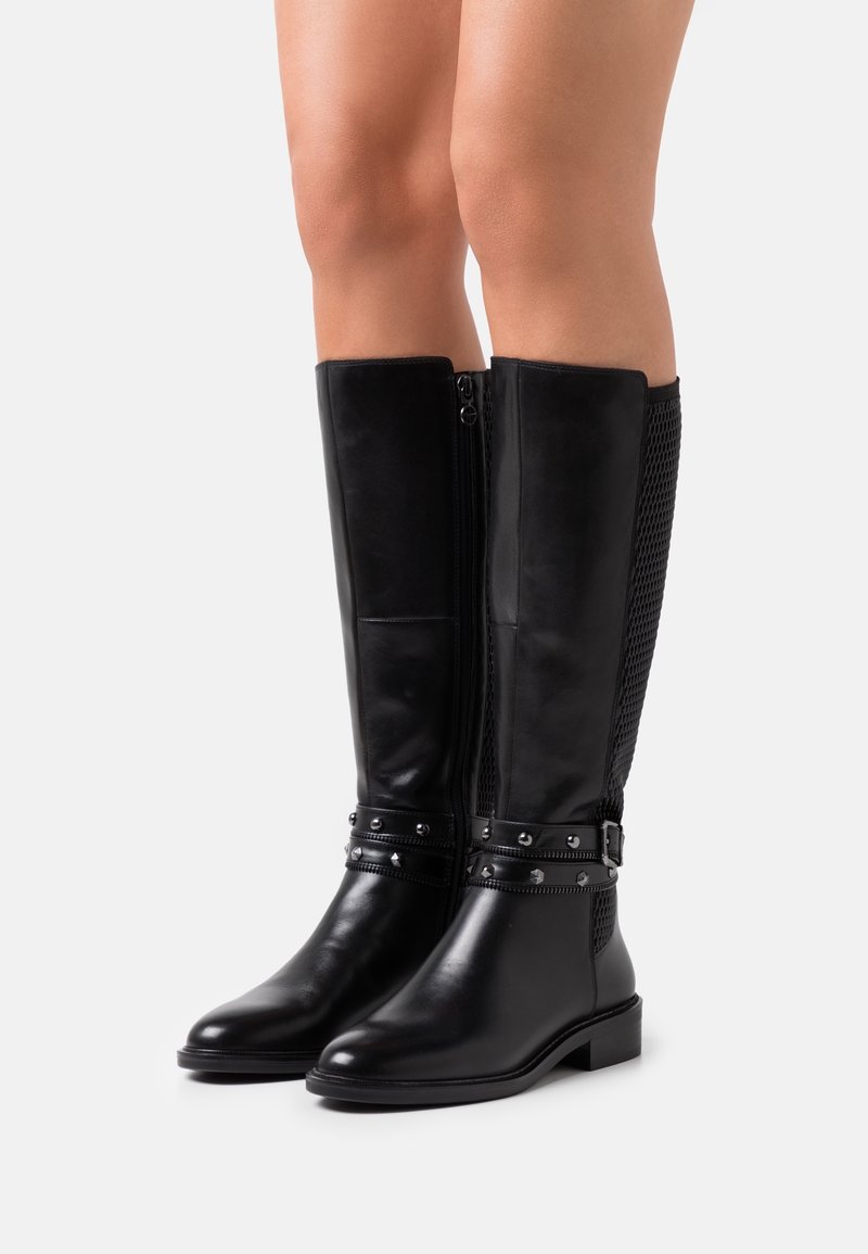 Bottes noires montant jusqu'au genou en cuir lisse avec un dos texturé. Dotées de clous argentés et d'une fermeture éclair latérale pour un enfilage facile.