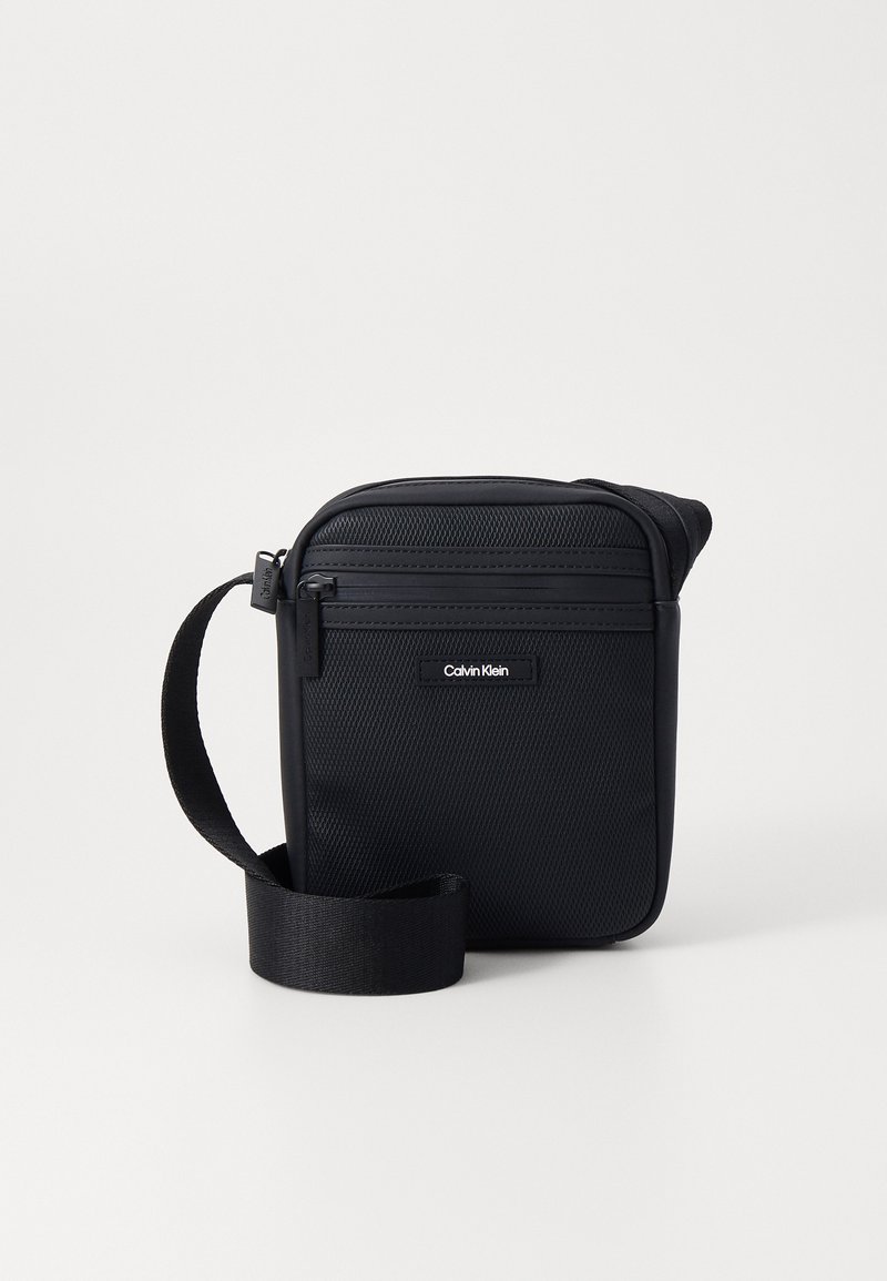 Black crossbody bag made of textured nylon with a smooth finish. Features a zippered closure, adjustable strap, and brand logo detail.