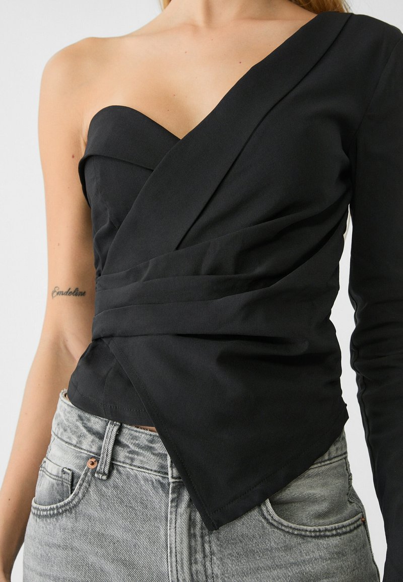 Top nero con design avvolgente asimmetrico; presenta una spalla e manica lunga. Realizzato in tessuto liscio, ha una vestibilità aderente e una cucitura curata.