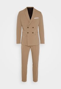 Rjav dvojno zapenjajoč blazer s temnimi gumbi, spremlja ozek kroj hlač. Ima žep z belim robcem kot poudarkom. Gladka tekstura.