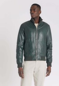 Groene leren bomberjack met een geribde kraag en manchetten, rits aan de voorkant en zijzakken, gecombineerd met lichte broeken.