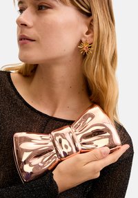 Metallic roséguldfärgad clutch med båtformat som hålls mot en svart glittrig topp, med en polerad yta och en upphöjd central knutdetalj.