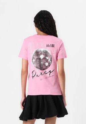 Camiseta de algodón rosa con un gran gráfico de bola disco plateada que dice "90's VIBE" y "Party" en negro y blanco, diseño de cuello redondo.