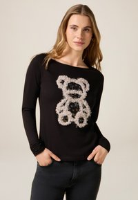 Czarna koszula z długim rękawem z teksturowanym, kremowym motywem niedźwiedzia ze błyszczącymi akcentami. Miękka tkanina z luźnym dekoltem i dopasowanymi rękawami.