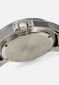 Roestvrijstalen horloge met een gepolijste en geborstelde afwerking. Heeft een ronde kast, een getextureerde kroon aan de zijkant en gegraveerde details op de achterkant.