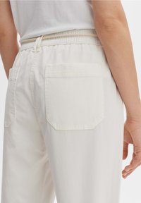 Witte katoenen broek met een elastische tailleband en een trekkoord. De achterkant heeft twee vierkante zakken met rechte stiksels en een gladde textuur.
