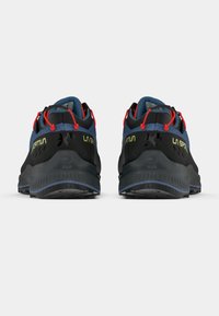 Zwarte en blauwe trailrunning schoenen met rode accenten, gestructureerde rubberen zolen en reflecterende details op een effen achtergrond.