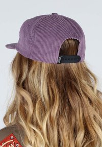 Casquette en velours côtelé violet avec une visière plate, dotée d'une fermeture à pression en plastique et d'une texture côtelée visible sur le tissu.