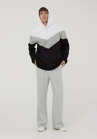 Felpa con cappuccio caratterizzata da un motivo a zig-zag bianco, grigio e nero, abbinata a pantaloni della tuta grigi chiari, realizzati in un morbido tessuto misto cotone.