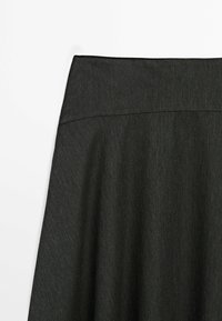 Gros plan sur la partie supérieure d'une jupe noire taille haute avec un tissu subtilement texturé et des lignes de couture nettes.