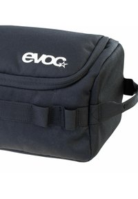 Borsa di tessuto nero con una texture liscia, caratterizzata da un logo bianco prominente, una patta superiore e fasce laterali per il trasporto o l'attacco.