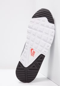 Nike sko-sula med en vit yta med upphöjda fyrkantiga mönster, svarta gummikanter och en framträdande röd swoosh-logotyp i en triangulär utskärning.