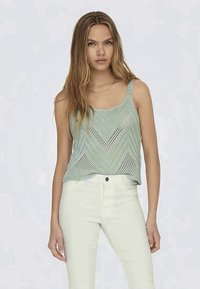 Hellgrünes gestricktes Tanktop mit Zickzackmuster, mit einem runden Ausschnitt und breiten Schulterträgern, kombiniert mit weißen Jeans.