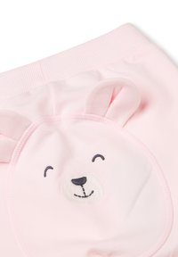Weiche rosa Babypants mit elastischem Bund haben einen lächelnden Bärenkopf-Patch und zwei kleine Stoffohren auf der Rückseite.