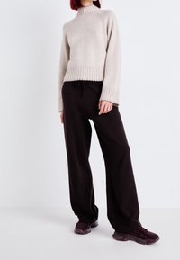 Pull beige en tricot avec col montant et ourlet côtelé, associé à un pantalon noir ample et des baskets texturées violettes.