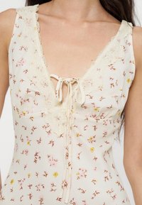Robe crème sans manches avec un petit motif floral rose et jaune, bordure en dentelle le long du décolleté en V profond et détail noué à l'avant.