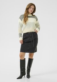 Zwarte denim kokerrok met een striktaille, gecombineerd met een crèmekleurige en grijs gestreepte gebreide trui. Kniehoge zwarte laarzen met hak maken de look compleet.