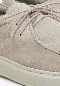 Beżowe zamszowe trampki z okrągłym noskiem, cienkimi beżowymi sznurowadłami i białą gumową podeszwą. Posiadają subtelne przeszycia i teksturowaną powierzchnię.