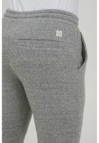Gray sweatpants with a textured knit finish, featuring a back pocket and an adjustable waistband with a branded label.