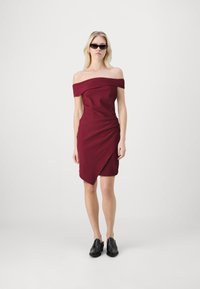 Burgundin väri off-the-shoulder mekko, jossa on pussitettua yksityiskohtaa ja epäsymmetrinen helma, yhdistettynä mustiin kenkiin ja tyylikkäisiin aurinkolaseihin.