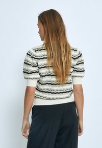 Kurzer, taillierter Pullover mit kurzen Ärmeln in einer cremefarbenen Basis, versehen mit gewellten schwarzen Streifen und strukturierten Details auf der Rückseite sowie geripptem Saum und Bündchen.